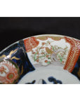 Close-up of red, green, and gold hand painted porcelain Japanese Imari bowl rim with floral and bird designs.