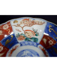 Close-up of red, blue, and gold porcelain Japanese Imari bowl with hand painted floral and landscape design.