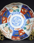 Colorful hand painted Japanese Imari porcelain bowl with floral and geometric patterns on a brass stand, close-up.