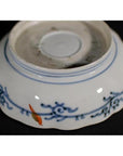 Blue and orange floral designs on white porcelain bowl, hand painted, seen on plain background.