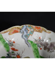 Close-up of a multicolored Imari porcelain bowl with scalloped rim, featuring gold, green, orange and blue floral and bird designs.