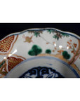 Red, green, and gold floral and geometric patterns on hand painted Japanese Imari porcelain bowl, close-up view.