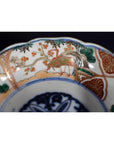 White porcelain Imari bowl with intricate green, gold, red, and blue floral and bird designs.