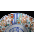 Close-up of a blue, red, green, and gold Imari porcelain bowl with hand-painted rim patterns.