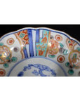 Close-up of a porcelain Japanese Imari bowl with vibrant red, blue, and green hand-painted patterns on the rim.