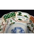Close-up of an antique Japanese Imari porcelain bowl with green, orange, and blue bird, tree, and geometric patterns.