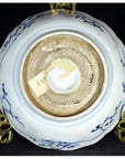 White and blue porcelain bowl base with sticker label on ornate metal stand, close-up.
