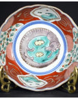 White and blue porcelain Imari bowl with hand painted dragon and cloud motifs on a decorative stand, close-up view.