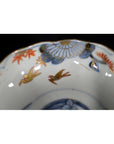 Close-up of blue, gold, and red hand painted porcelain Imari bowl with floral patterns and two birds.