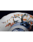 Close-up of a blue, orange, and gold porcelain Japanese Imari bowl with hand painted floral and tree motifs.