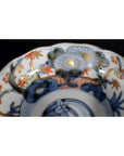 Blue, gold, and orange Imari porcelain bowl with hand painted floral and leaf patterns on rim, close-up.