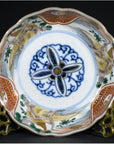 Close-up of antique Japanese Imari porcelain bowl with blue floral center and ornate gold, red, and green rim designs.