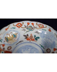 Close-up of a Japanese Imari porcelain bowl, hand painted with red, blue, green, and gold floral and animal designs.