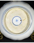 White and blue porcelain bowl underside on brass stand, hand painted in Japanese Imari style, indoor setting.
