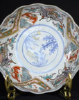 Red, blue, and gold hand-painted Japanese Imari porcelain bowl with crane and floral designs on brass stand.