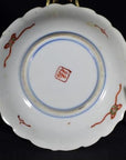 Close-up of an antique hand painted Japanese Imari porcelain plate with red and green designs on white background.