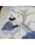 Close-up of blue and gold Imari porcelain plate featuring hand-painted pagoda, bridge, tree, and water.