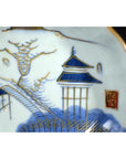 Close-up of blue and gold hand painted porcelain Japanese Imari plate with scenic landscape details.