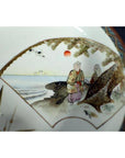 Close-up of antique hand-painted Japanese Kutani porcelain bowl with two figures, trees, red sun, and distant buildings.