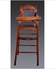 Brown rattan and wood antique highchair with woven seat, set against a dark background.