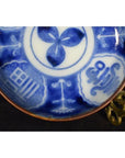 White porcelain Igezara transferware plate with intricate patterns and calligraphy on a brass stand.