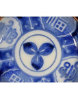 White porcelain Igezara transferware plate with central three-petal floral motif and abstract patterned rim, close-up.
