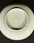 Close-up of the base of a round white ceramic Antique Igezara Transferware plate against a dark background.