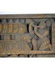 Brown Sheesham wood temple plaque with ornate carvings and kneeling figure blowing a horn, early 20th century.