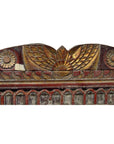 Close-up of gold and red hand carved antique Indian wall ornament with floral patterns and central wing-like motif.