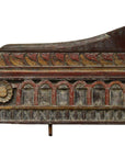 Close-up of antique Indian hand-carved wall ornament with red, yellow, and brown floral arches and aged paint.