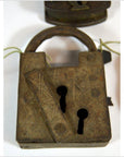 Antique metal Indian lock with two keyholes and engraved patterns on a white background.
