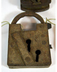 Antique metal Indian lock with two keyholes and engraved patterns on a white background.