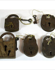 Close-up of five antique metal Indian locks with attached keys on strings, displayed on a white surface.