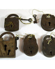 Close-up of five antique metal Indian locks with attached keys on strings, displayed on a white surface.