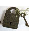 Close-up of an antique metal Indian lock with key tied by string, placed on a white surface.