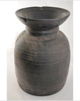 Close-up of a large, dark, round antique Indian metal milk storage container with ridged horizontal lines and wide neck.