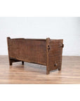 Weathered brown wooden planter with chiseled texture on a wooden floor against a white brick wall indoors.