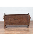 Brown weathered wooden planter with chiseled texture on wood floor next to a white brick wall indoors.