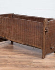 Brown weathered wooden planter with chiseled texture, open top, sitting on a wooden floor.