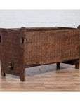Brown weathered wooden planter with chiseled texture on a wooden floor beside a white brick wall indoors.