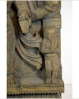 Brown Sheesham wood carving with small praying figure next to larger draped statue, close-up view.