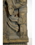 Brown Sheesham wood carving with small praying figure next to larger draped statue, close-up view.