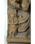 Brown Sheesham wood carving of small praying figure beside larger draped figure, Indian antique style, close-up.