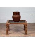 Brown wooden side table with window grate top and baluster legs against a white brick wall indoor setting.