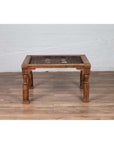 Brown wood side table with window grate top and turned baluster legs, on wood floor near white brick wall indoors.