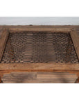 Brown wooden side table with window grate top and turned baluster legs on a wood floor against a white wall indoors.