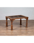 Brown wooden side table with window grate top and turned baluster legs on a wood floor against a brick wall.