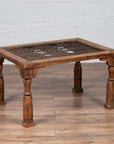 Brown wooden Indian side table with window grate top and turned baluster legs on wooden floor against white wall.