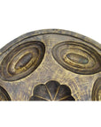 Close-up of an antique wooden Indonesian cake mold with carved circular and floral patterns on a textured surface.