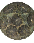 Close-up of weathered greenish antique Indonesian cake mold with five raised floral motifs, metal surface visible.
